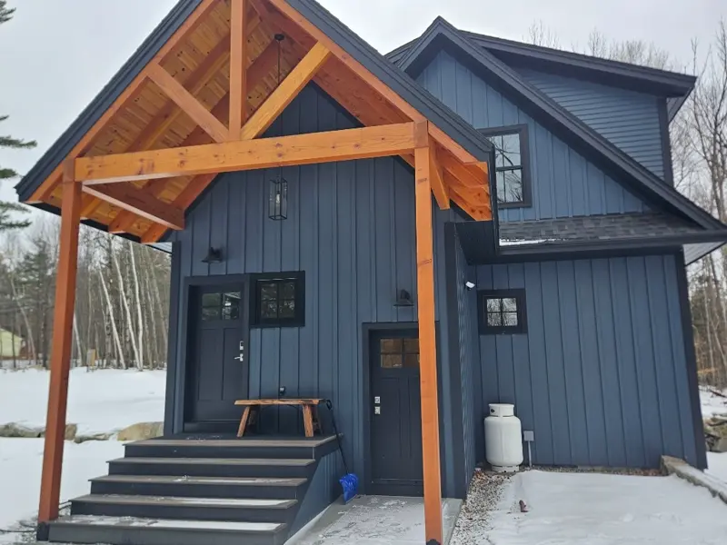 Stunning modern blue custom home entryway with timber frame porch and winter scenery